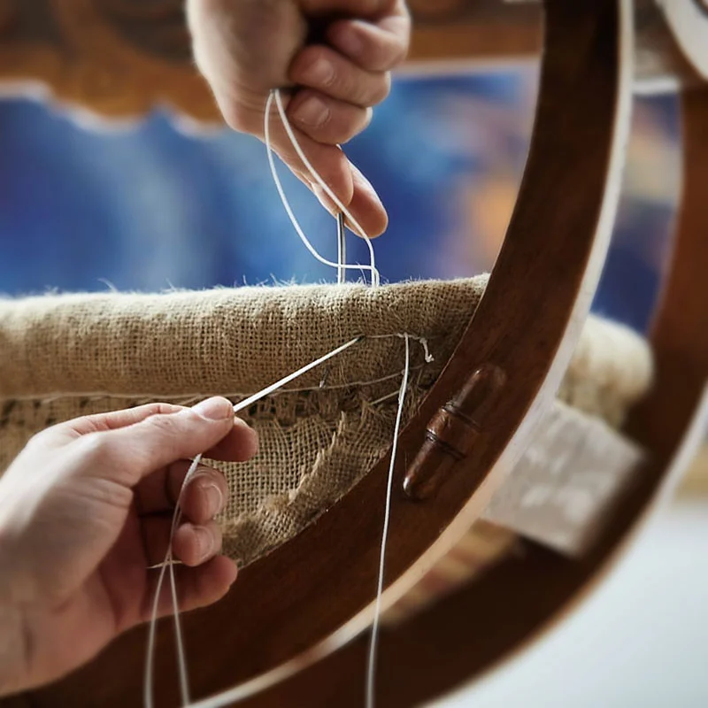 Hände die an einem alten Stuhlgestell Jutenstoff vernähen