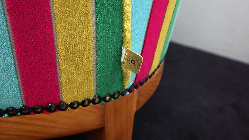 Detailaufnahme eines Möbels mit Rot-gelben-grünen Streifen und Bronze farbenen Deutschmann Schild