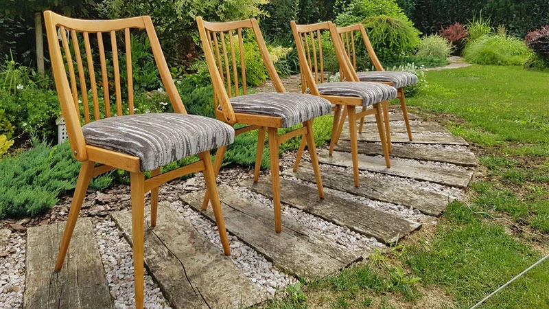 Vier Esszimmerstühle aus hellem Holz mit grauem Bezug auf einem Kieselstein-Holz-Weg in einem Garten