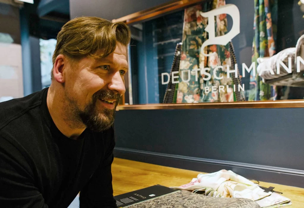 Karsten Deutschmann mit schwarzem Shirt im Vordergrund, Fensterscheibe mit dem Deutschmann Logo im Hintergrund